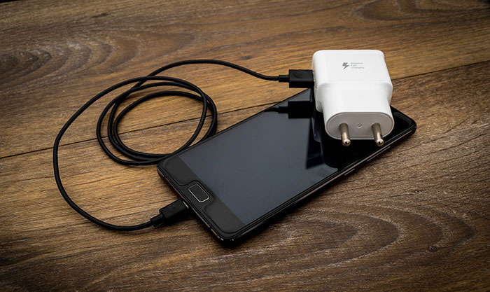 Smartphone with charger on wooden surface, illustrating useful tips for an elevated and stress-free hotel stay.