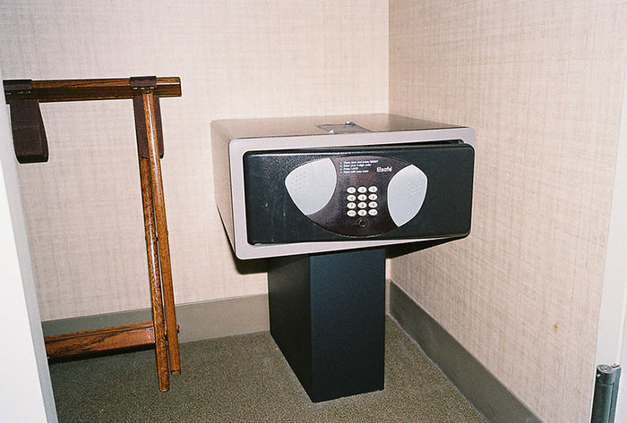 Hotel room safe on a pedestal next to a wooden luggage rack, illustrating tips for an elevated and stress-free hotel stay.