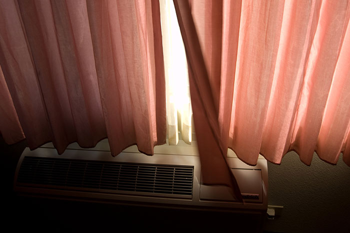 Hotel room air conditioner below partially opened curtains, illustrating tips for a more elevated and stress-free hotel stay.