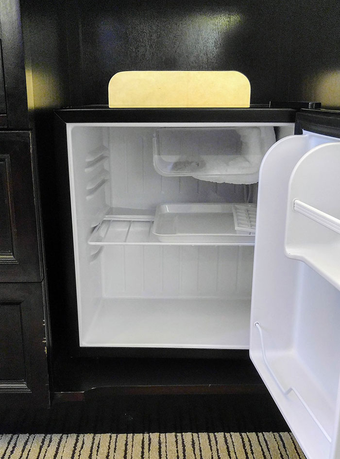 Open empty hotel mini fridge with ice compartment inside dark wooden cabinet, illustrating hotel stay tips for a stress-free experience.