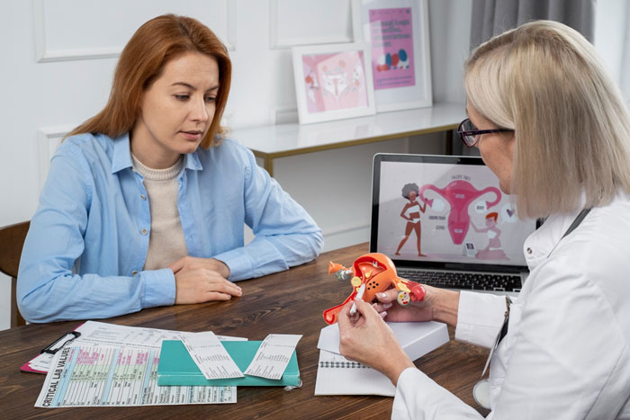 Woman discussing cervical cancer diagnosis with a doctor, who is showing a uterus model and a diagram on a laptop.
