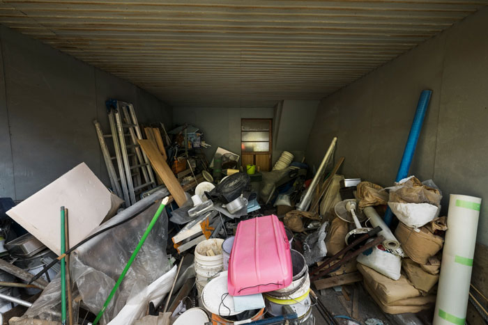 A messy room overflowing with varied items like ladders, wood, buckets, and a pink container, depicting a hoarder's house.