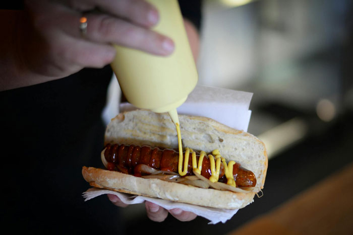 Man squeezing mustard on a hot dog in a bun, symbolizing a man's outburst over wife not liking mustard.