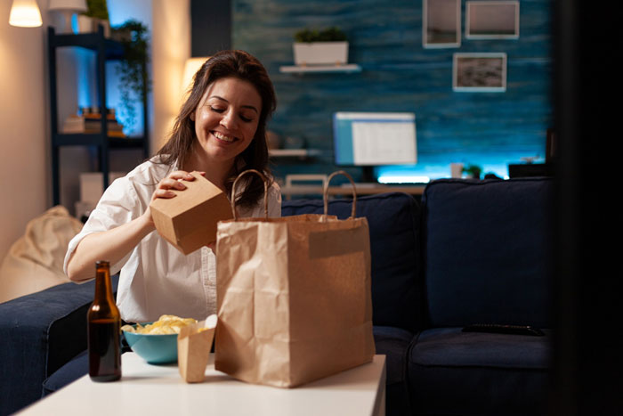Woman smiling while unpacking takeout food at home, relating to a man&rsquo;s outburst over mustard dislike.