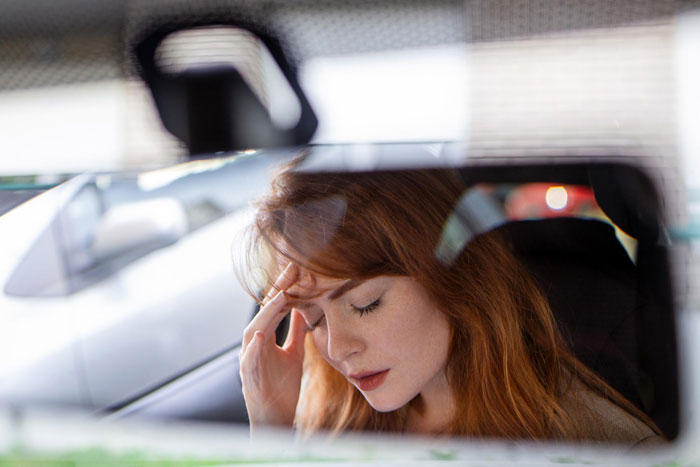 Woman with red hair sitting in car, holding forehead in frustration, reflecting a man&rsquo;s outburst over mustard dislike.