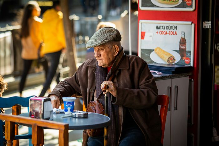 Elderly man sitting at a cafe table outdoors, reflecting on satisfying karma moments in everyday life.