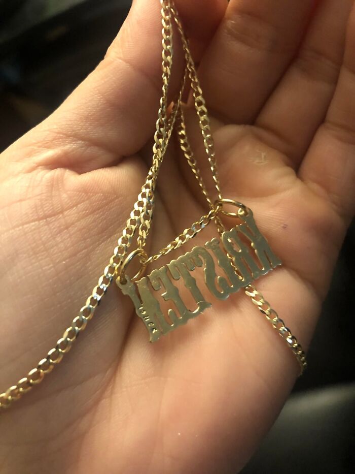 Close-up of a hand holding a gold nameplate necklace, one of the strange and disturbing things found in elevator pits.