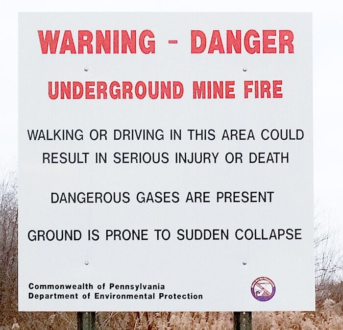 Warning sign about underground mine fire hazards, highlighting dangerous gases and risk of sudden collapse in a horrifying historical context.