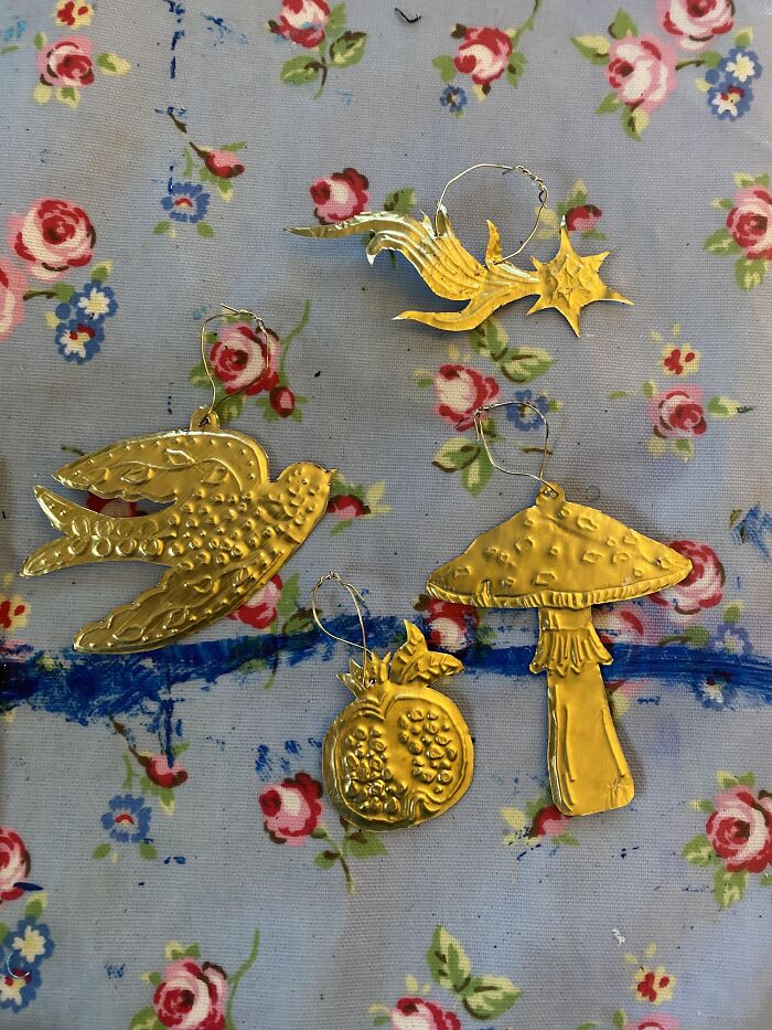 Four golden metal ornaments: a bird, a shooting star, a mushroom, and a pomegranate, showcasing creative people's artistry.