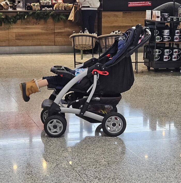 A child sleeps awkwardly in a stroller at an airport, illustrating a chaotic place for tired travelers.