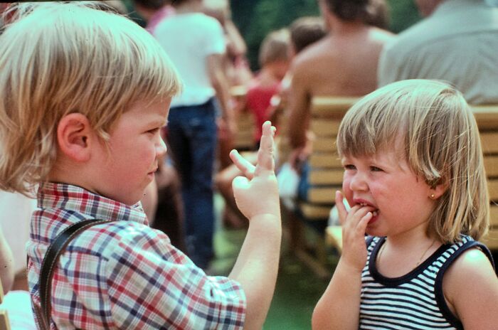 Two young children interacting outdoors during a family gathering, illustrating normal family activities now seen as bizarre.