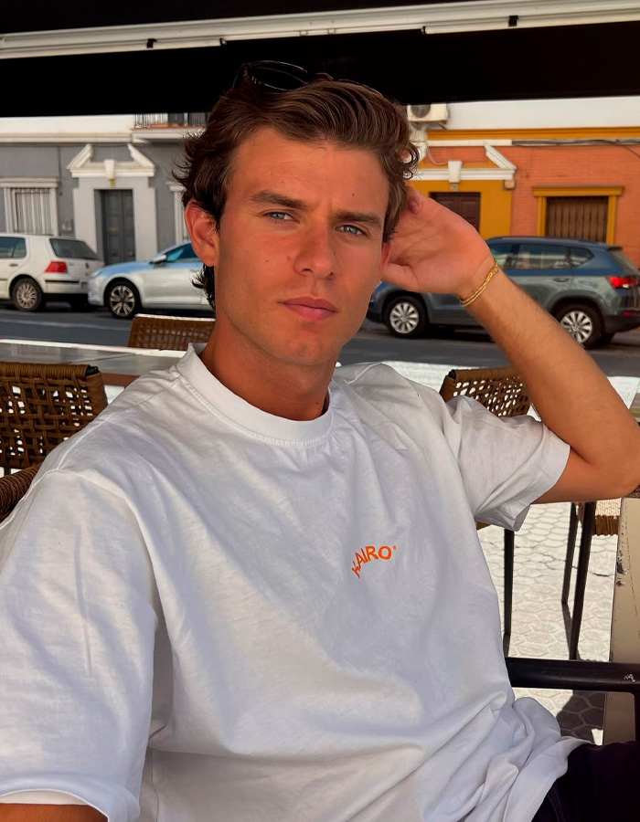 Jovem de cabelos castanhos e camisa branca sentado ao ar livre em uma cidade espanhola, ligado ao mistério da gostosa procissão da Páscoa espanhola.