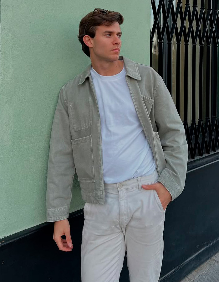 Jovem encostado na parede verde, vestido com jaqueta casual e calça branca, relacionado à gostosa no tema procissão de Páscoa espanhola.