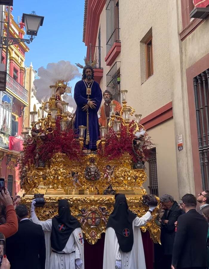 Procissão de Páscoa espanhola com carros alegóricos religiosos ornamentados e participantes em trajes tradicionais durante a celebração da Semana Santa.