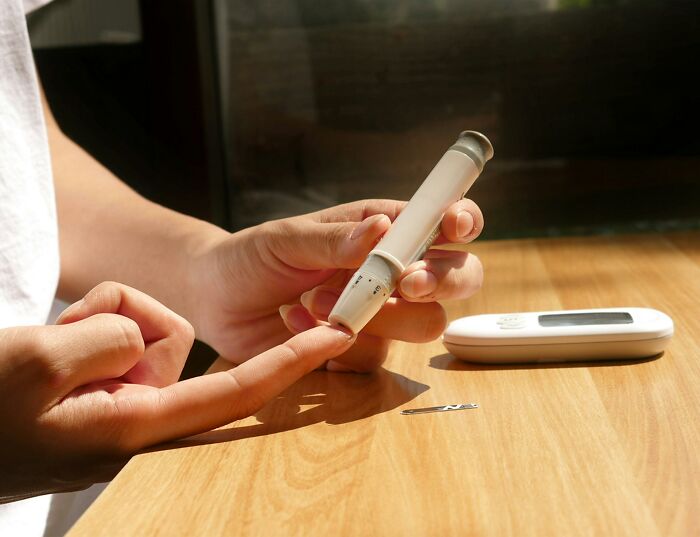 Person testing blood sugar with a lancet device and glucometer on wooden table showing medical facts concept