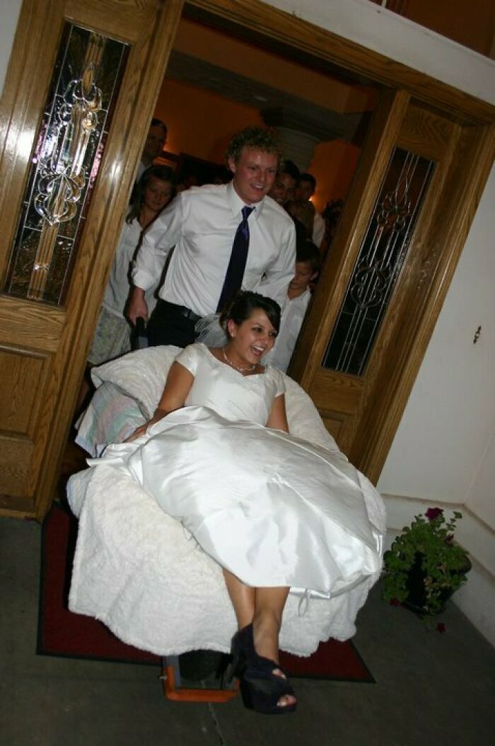 Bride in wedding dress being pushed on a chair by groom, a tacky and trashy wedding moment with guests watching.