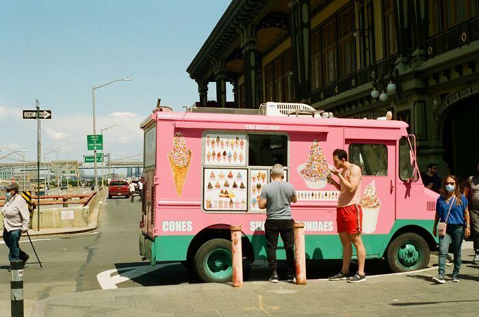 A pink and teal ice cream truck with customers on a city street. This is one of many disturbing sounds from daily life.