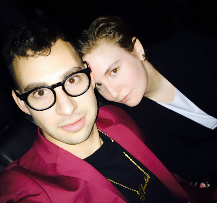Lena Dunham wearing black next to a man in glasses and a maroon jacket, highlighting peak main character syndrome theme.