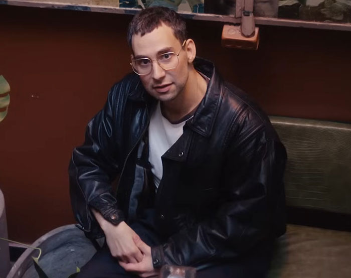 A man wearing glasses and a black leather jacket sitting indoors, illustrating Peak Main Character Syndrome concept.