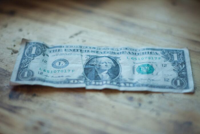Crumpled one dollar bill on a wooden table, illustrating financial challenges faced by gynecologists in their career path.