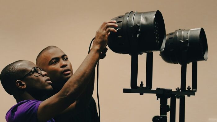 Two men adjusting studio lighting equipment, illustrating jobs that AI can’t touch in creative and technical fields.