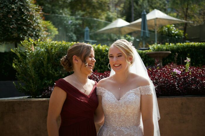 Bride in a wedding dress and bridesmaid smiling outdoors, capturing a moment from a wedding guest's future breakup story.