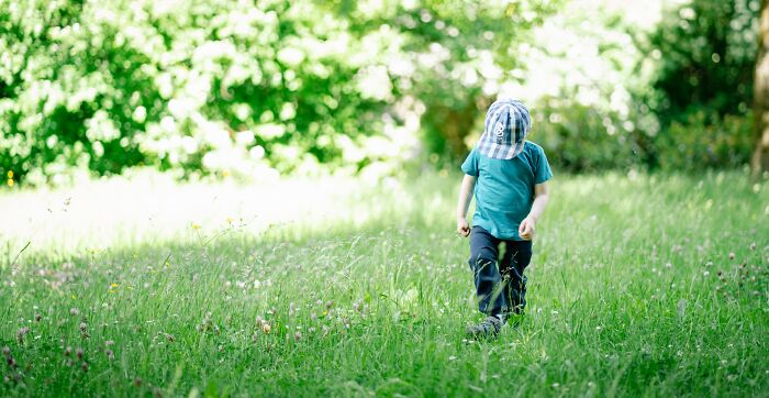 Young child wearing a cap walking alone in a green field, illustrating parenting tips and tricks outdoors.