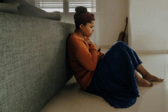 Young woman sitting on floor by couch, looking thoughtful and reflective in a quiet room, illustrating karma's impact.