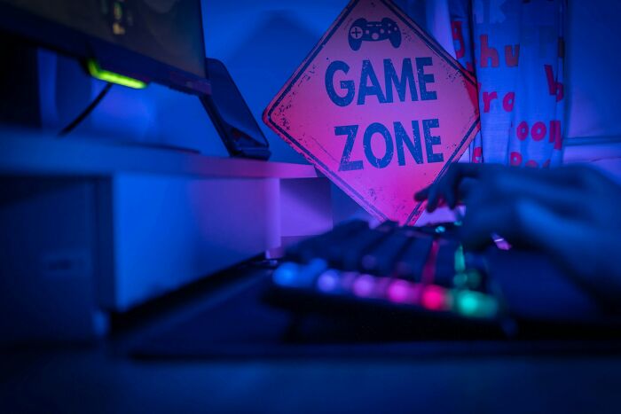 Hands typing on a colorful keyboard in a dimly lit room with a game zone sign, illustrating random life decisions.
