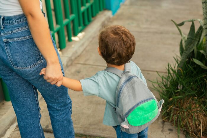 Child with backpack holding an adult's hand walking on a sidewalk, illustrating moments of weaponized incompetence.
