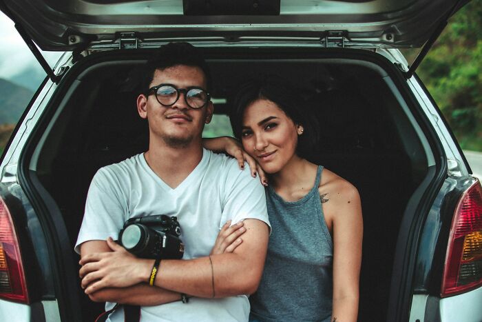 Young couple sitting in a car trunk, illustrating random life decisions leading people to the right place through honest stories.