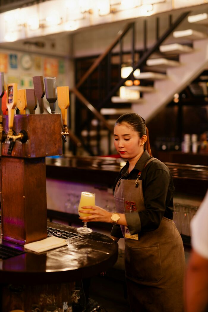 A woman, wearing an apron, pours a drink at a bar. Many people rage quit their jobs for various reasons.