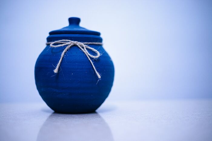Blue ceramic jar with a twine bow, photographed on a reflective surface with a light blue background representing TSA confiscated items.