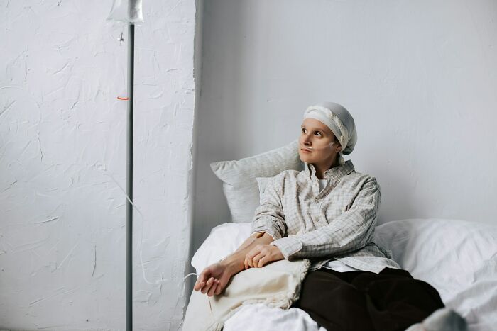 Woman with headscarf receiving IV treatment, sitting on bed and looking away, representing terrifying statistics on health challenges.