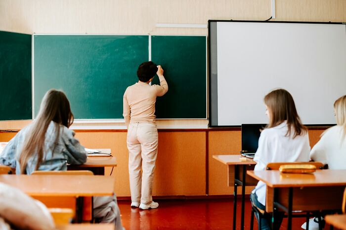 Teacher writing on a chalkboard in a classroom while students sit at desks, reflecting stories of dealing with horrible bullies.