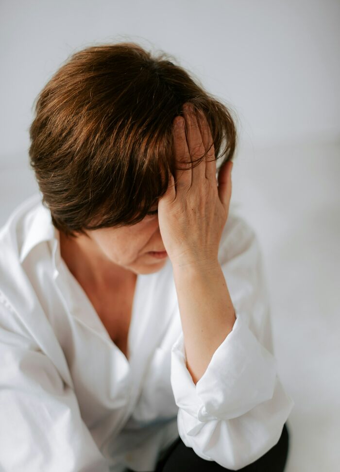 Middle-aged woman in white shirt looking distressed while holding her forehead, reflecting on dark family secrets.