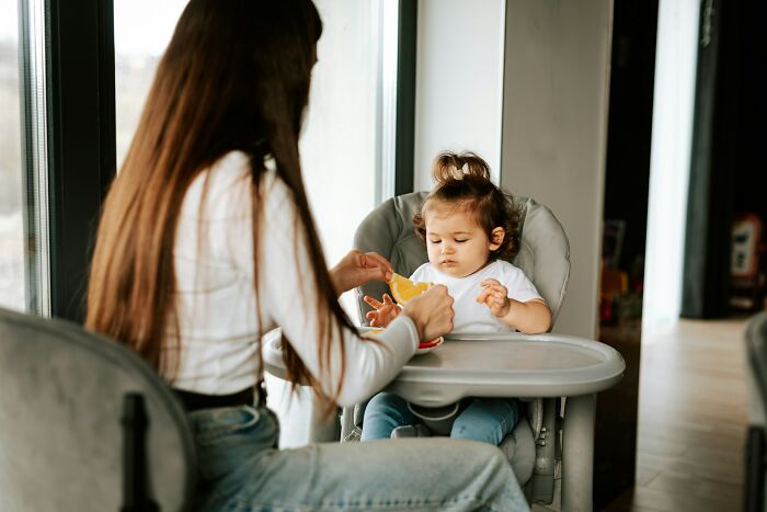 Woman feeding toddler in high chair, capturing a moment that reflects accidental message mishaps and mortifying experiences.
