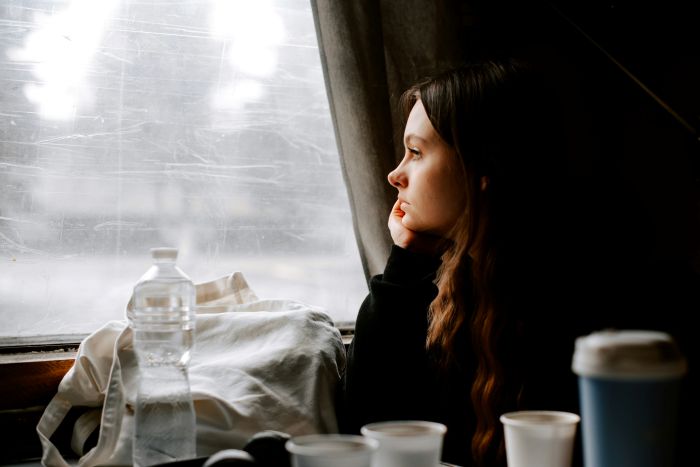 A young woman with long hair looking pensively out a window. Her best friend skipped her wedding.