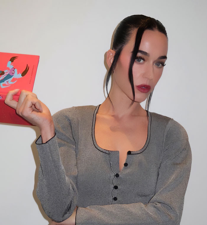 Woman with dark hair and red lipstick wearing a gray top, posing while holding a red card, related to club manager revelations. Woman with dark hair and red lipstick wearing a gray top, posing while holding a red card, related to club manager revelations.