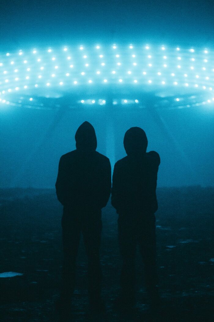 Two hooded figures stand in the dark under a glowing ring of lights, evoking horrifying historical facts atmosphere.