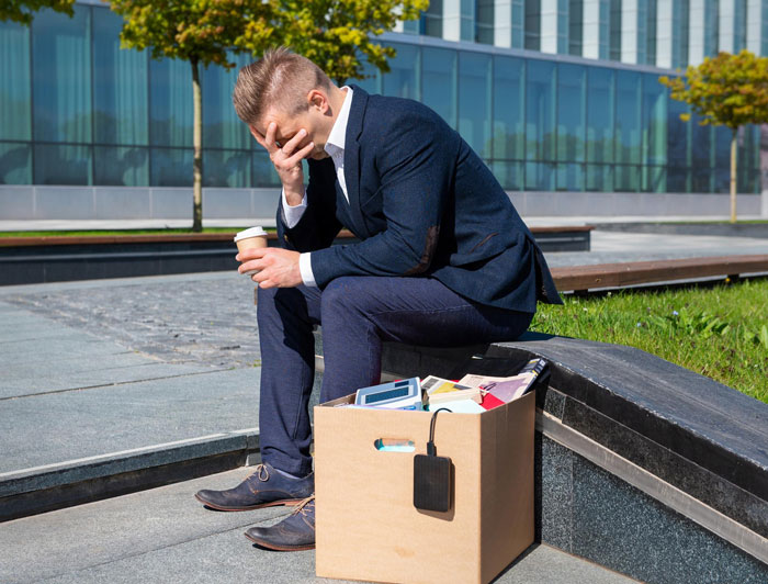 Man sitting outside an office building looking stressed with a box of belongings after being fired from work. Man sitting outside an office building looking stressed with a box of belongings after being fired from work.