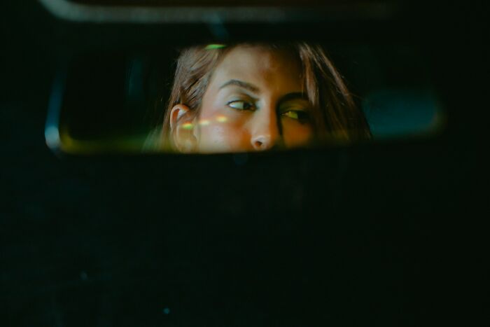 Woman’s face partially visible in a rearview mirror, capturing a candid moment related to bachelor and bachelorette parties.