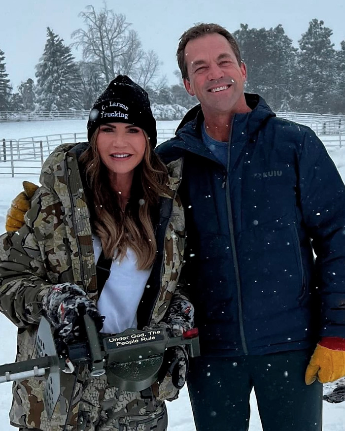 Kristi and Bryon Noem outdoors in snow with camo jacket and blue coat amid $2.6 million debt scandal and luxury spending questions