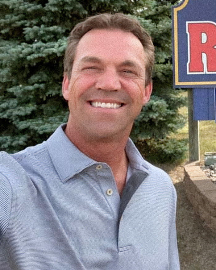 Man smiling outdoors in a light blue shirt, related to Kristi and Bryon Noem’s $2.6 million debt scandal coverage.