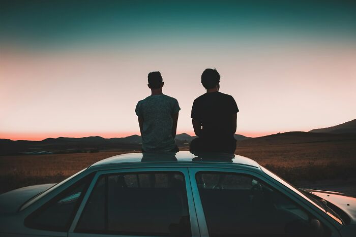 Two people sitting on a car roof at sunset reflecting on past experiences with former bullies who made their lives difficult.