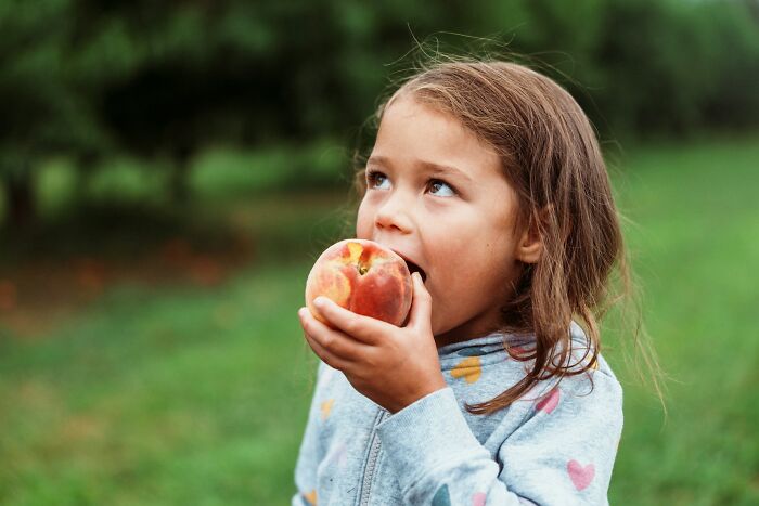 Young girl eating a peach outdoors, illustrating one of the normal family activities people now find bizarre.