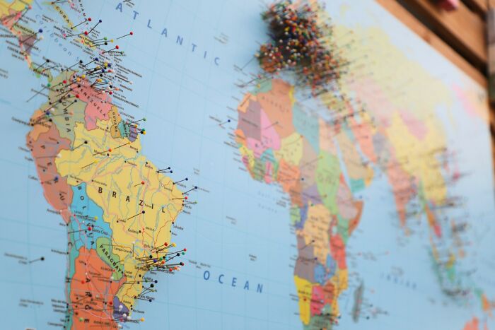 A close-up of a world map with colorful pushpins marking various locations, useful for a geography quiz on pound sterling.