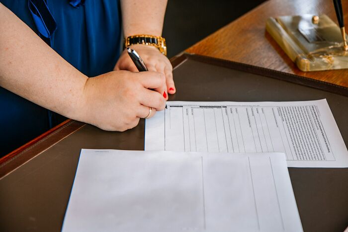 A person with red nail polish and a gold watch is signing a document, relating to MIL stories.