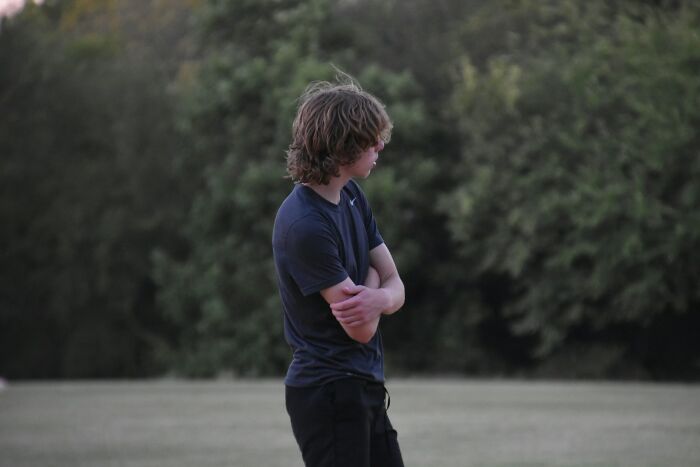 Teen boy standing alone in a park looking away, reflecting on experiences with horrible bullies and personal challenges.