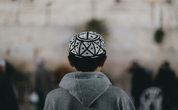 Person wearing a patterned cap and gray hoodie facing a stone wall, illustrating themes of karma coming in all forms.